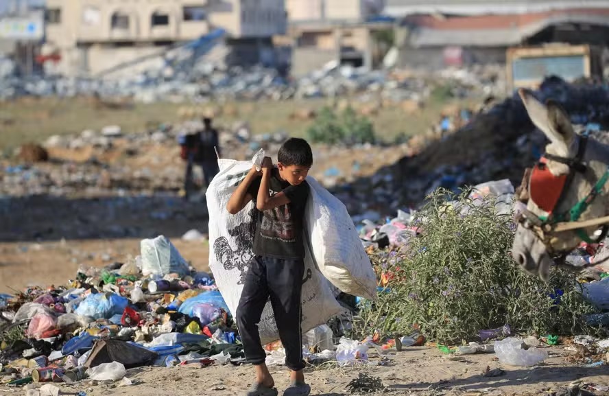 Jovem palestino carregando sacolas caminha perto de um depósito de lixo no campo de refugiados de al-Maghazi, no centro da Faixa de Gaza 