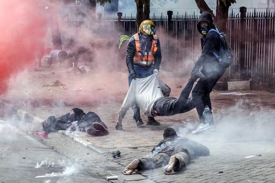 Manifestantes carregam um homem ferido enquanto outros estão caídos no chão em frente ao Parlamento do Quênia