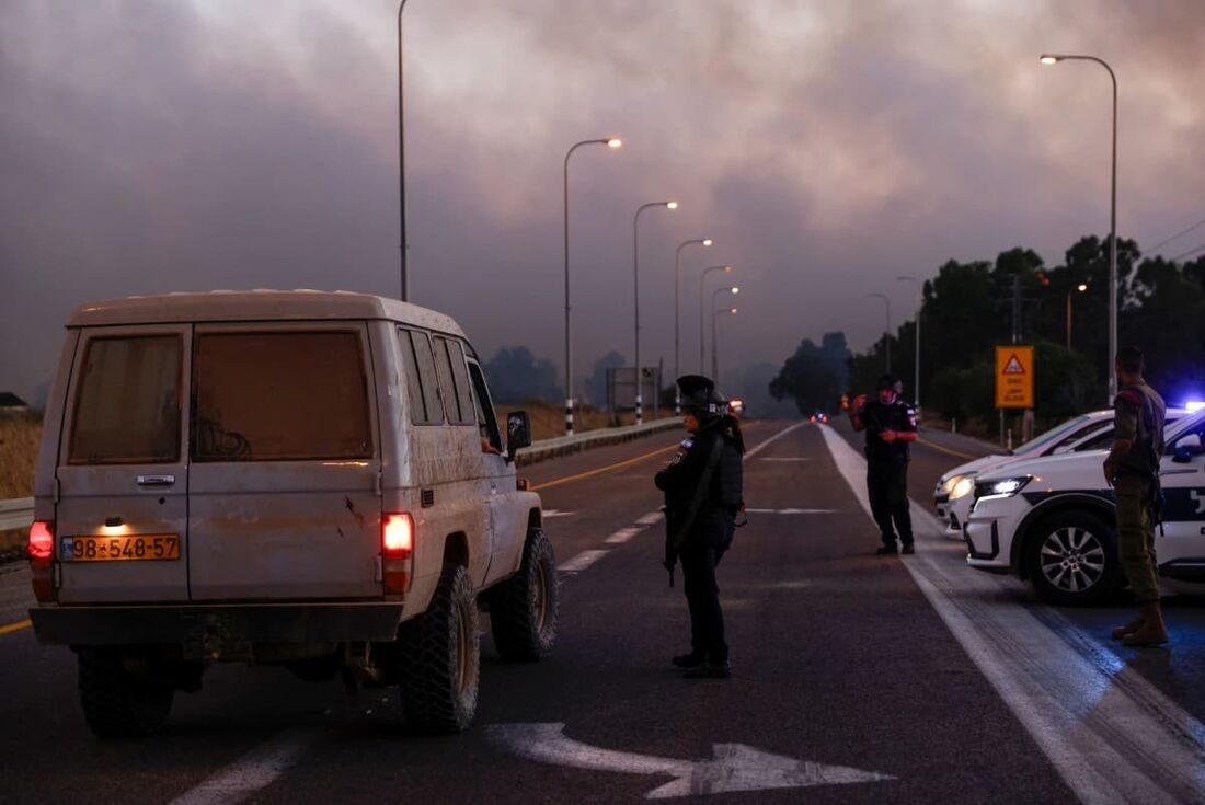 A polícia israelense protege uma estrada enquanto a fumaça sobe após o lançamento de foguetes do sul do Líbano 