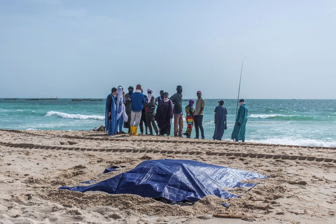 Espectadores olham para corpos cobertos de migrantes que morreram em um naufrágio na costa da Mauritânia enquanto estavam em uma praia fora de Nouakchott 