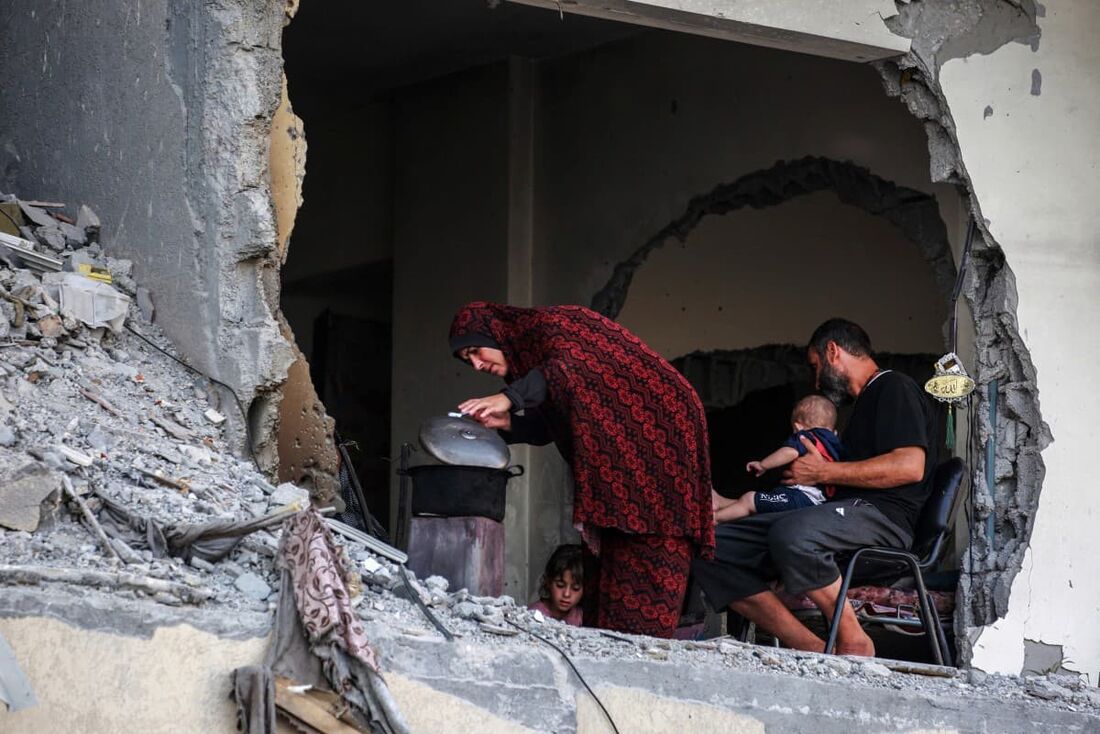 Uma família palestina se reúne em torno de um fogão a lenha improvisado em um prédio danificado em Khan Yunis, no sul da Faixa de Gaza