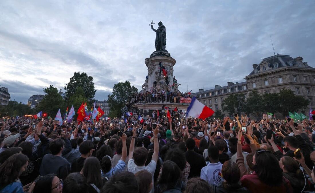 Participantes agitam bandeiras tricolores francesas durante um comício na noite das eleições legislativas francesas