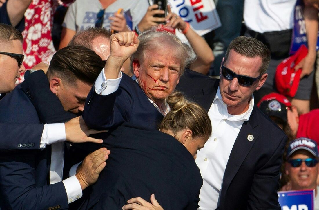 O candidato republicano Donald Trump com sangue no rosto cercado por agentes do serviço secreto enquanto é retirado do palco em um evento de campanha