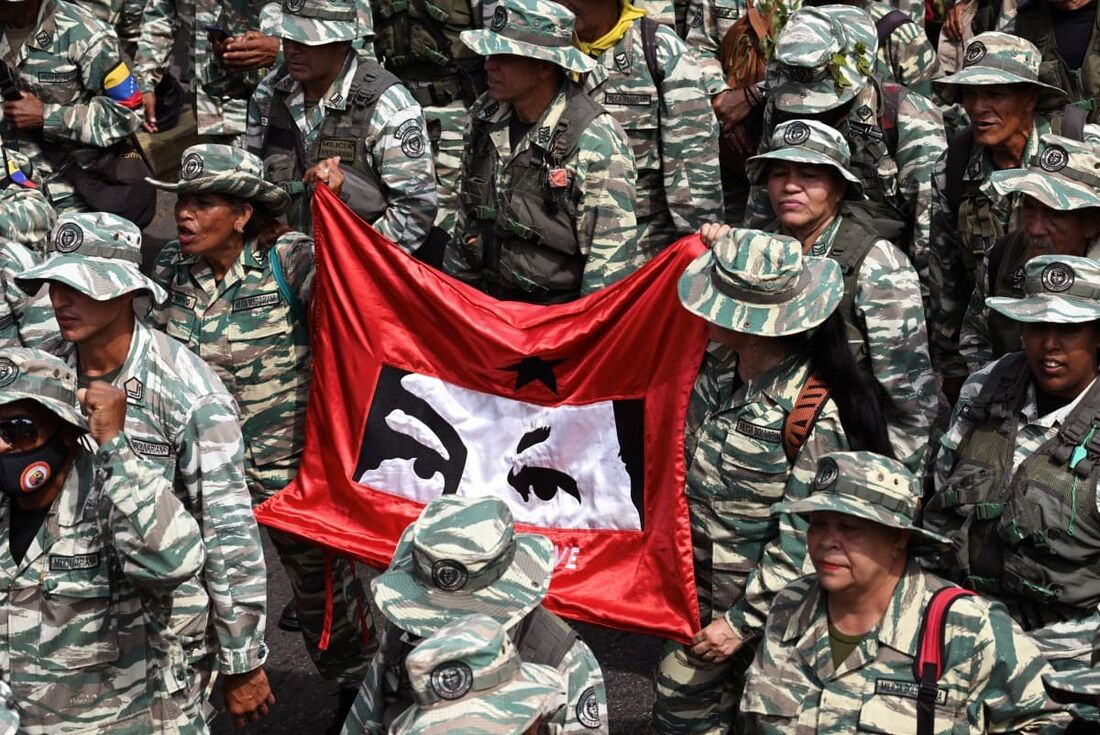 Membros da milícia bolivariana seguram uma bandeira com a imagem dos olhos de Chávez durante uma marcha para comemorar o 21&ordm; aniversário do retorno do falecido presidente venezuelano Hugo Chávez 