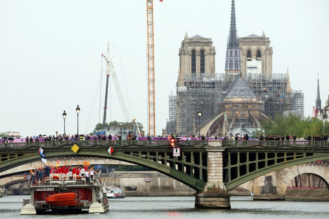 Atletas da delegação da Espanha navegam em um barco ao longo do rio Sena no início da cerimônia de abertura dos Jogos Olímpicos de Paris 2024 em Paris, enquanto a Catedral de Notre-Dame é vista ao fundo.