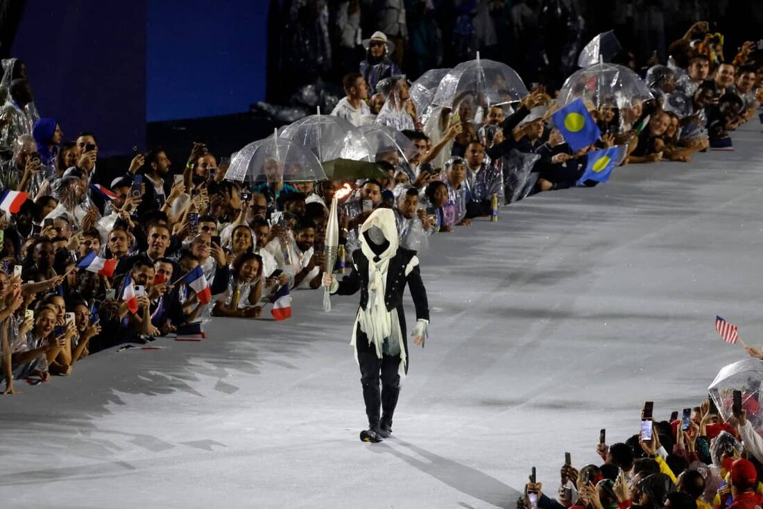 Mascarado com a tocha olímpica durante a cerimônia de abertura dos Jogos de Paris