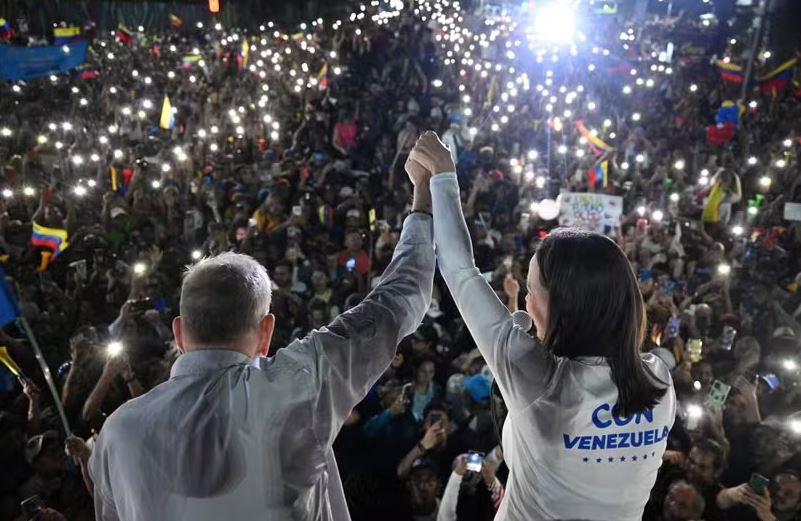 O candidato presidencial da oposição venezuelana Edmundo González Urrutia (E) e a líder da oposição María Corina Machado acenam aos apoiadores durante comício de encerramento de campanha em Caracas 