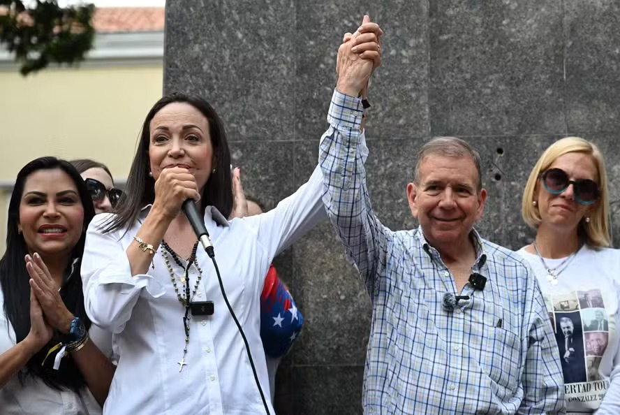 A líder da oposição Maria Corina Machado (E) segura as mãos do candidato presidencial venezuelano Edmundo Gonzalez Urrutia enquanto discursa durante encontro com fiéis cristãos em Caracas 