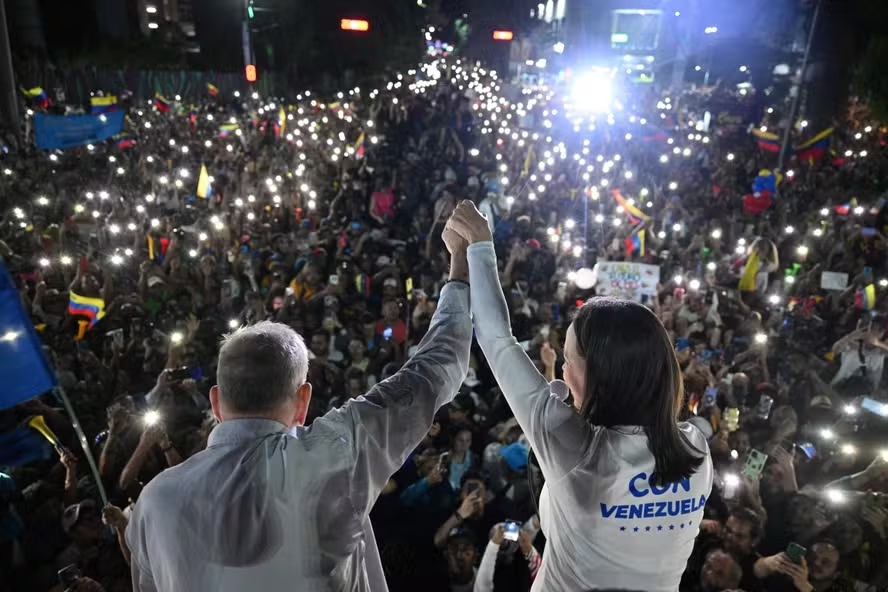 O candidato presidencial da oposição venezuelana Edmundo González Urrutia (E) e a líder da oposição María Corina Machado acenam aos apoiadores durante comício de encerramento de campanha em Caracas 