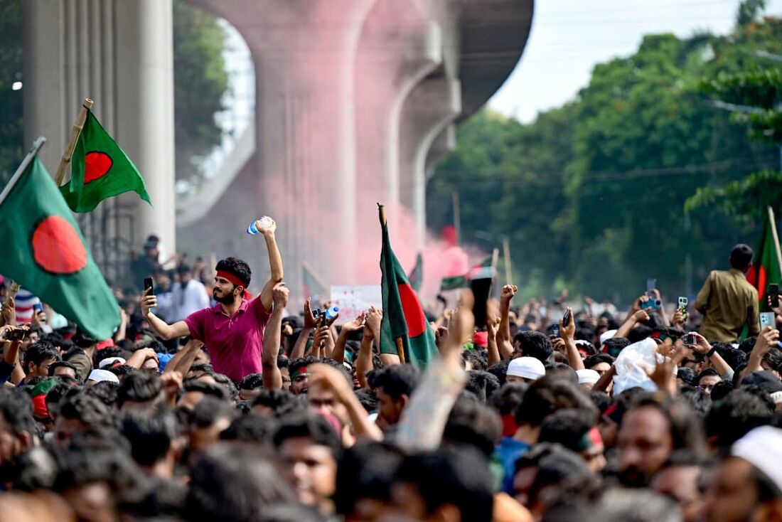 Manifestantes antigovernamentais agitam a bandeira nacional de Bangladesh enquanto comemoram