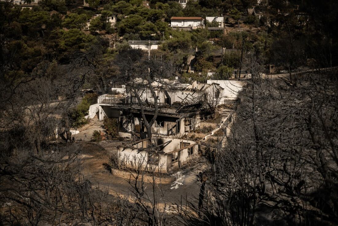 Esta fotografia mostra uma vista de casas queimadas após um incêndio florestal que atingiu os subúrbios do nordeste de Atenas