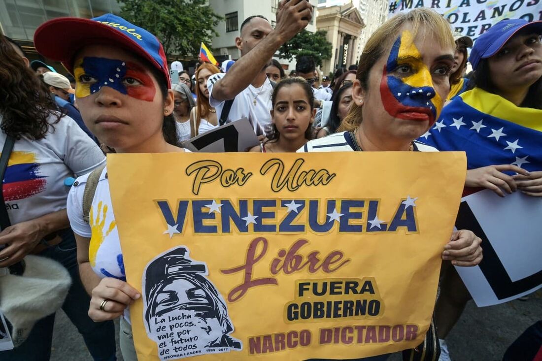 Dois cidadãos venezuelanos, com os rostos pintados com a bandeira da Venezuela, seguram uma faixa contra o presidente venezuelano Nicolás Maduro durante um protesto em apoio à oposição venezuelana 