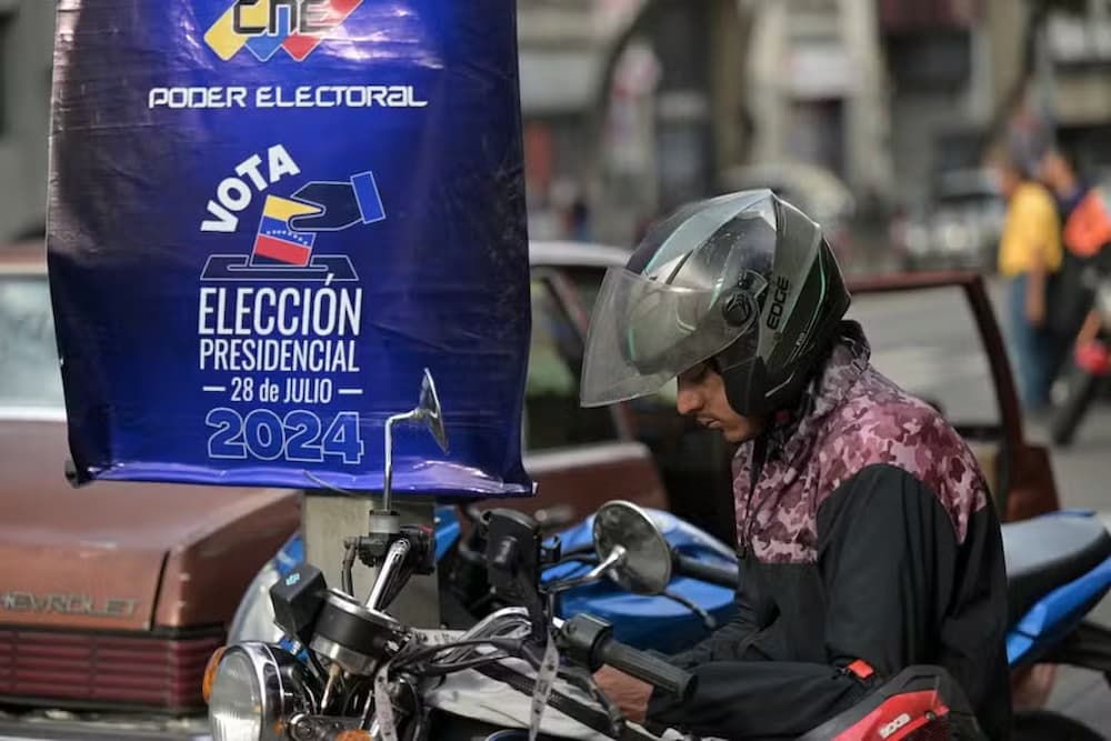 Um motociclista olha seu celular em frente a um cartaz do Conselho Nacional Eleitoral (CNE)