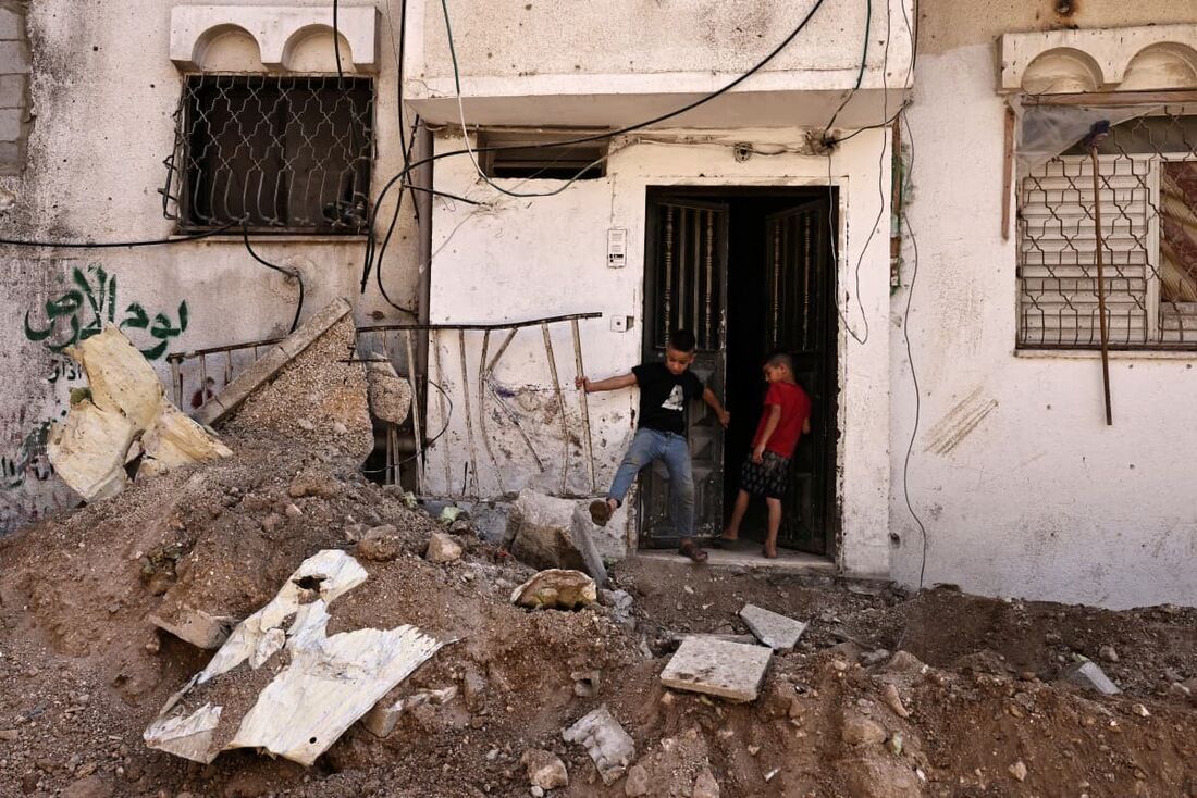 Crianças estão na porta de um prédio em uma rua onde escavadeiras israelenses haviam raspado o asfalto durante um ataque do exército, no campo de refugiados de Tulkarm, na Cisjordânia ocupada