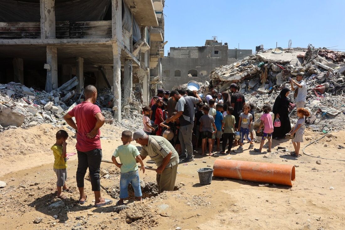 Um homem escava enquanto crianças se reúnem em um ponto de distribuição de alimentos em meio aos escombros de edifícios destruídos durante o bombardeio israelense, no campo de Jabalia para palestinos deslocados