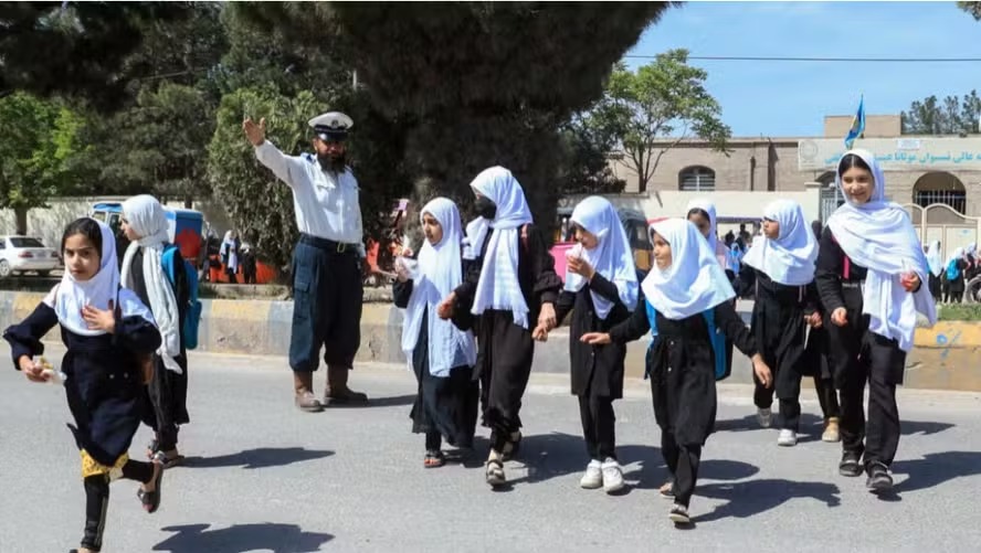 Um policial afegão para o trânsito enquanto estudantes atravessam uma rua em frente a uma escola em Herat em 16 de abril de 2024