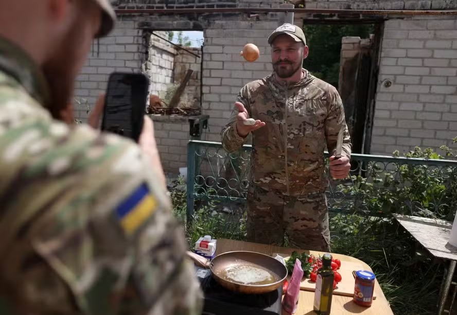 O militar e influenciador ucraniano Ruslan Mokrytskyi cozinha macarrão enquanto seu colega soldado grava um vídeo dele para o Tik Tok em um local não revelado na região de Donetsk, em 27 de julho de 2024 