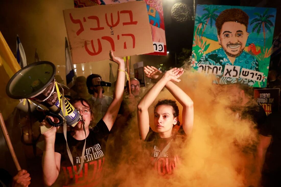 Manifestantes gritam slogans e reagem em meio à fumaça de sinalizadores durante um protesto antigovernamental pedindo ação para libertar os reféns 