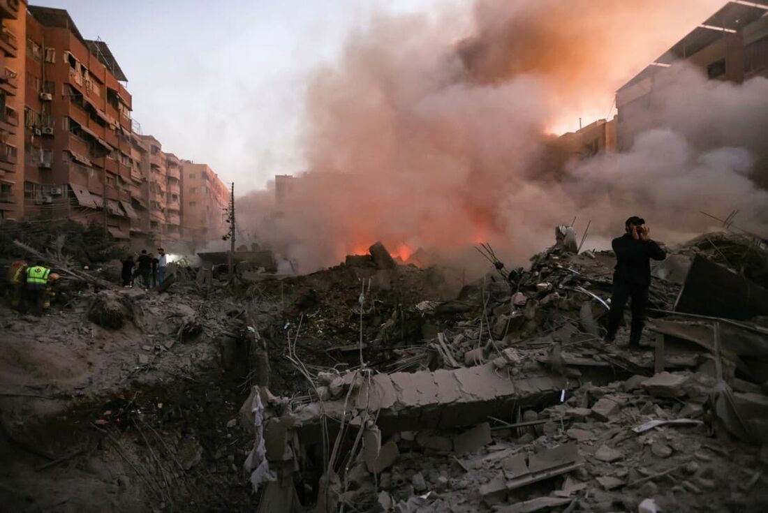  Pessoas e equipes de resgate se reúnem perto dos escombros fumegantes de um prédio destruído em um ataque aéreo israelense no bairro de Haret Hreik, nos subúrbios ao sul de Beirute