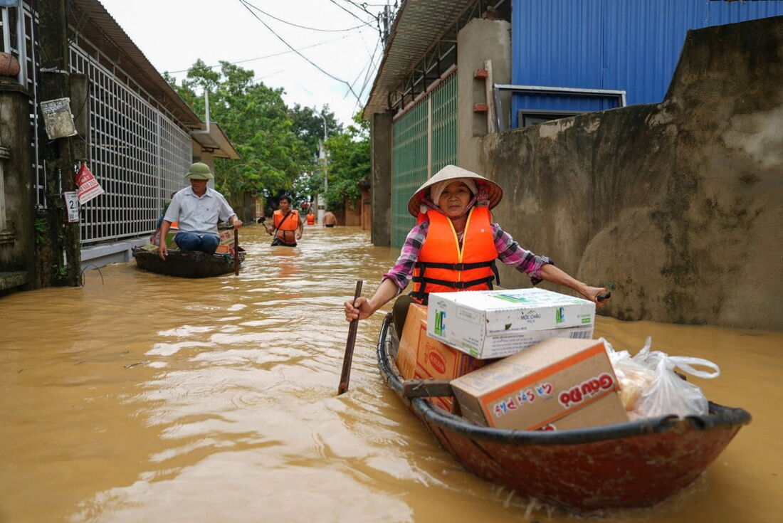 Uma mulher rema um barco ao longo de uma rua inundada carregando pacotes de comida na província de Thai Nguyen em 10 de setembro de 2024, após o Tufão Yagi atingir o norte do Vietnã