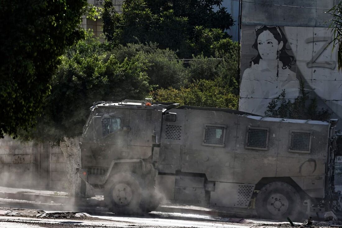 Um veículo do exército israelense passa por um antigo outdoor durante um ataque do exército israelense em Tulkarem, no norte da Cisjordânia ocupada