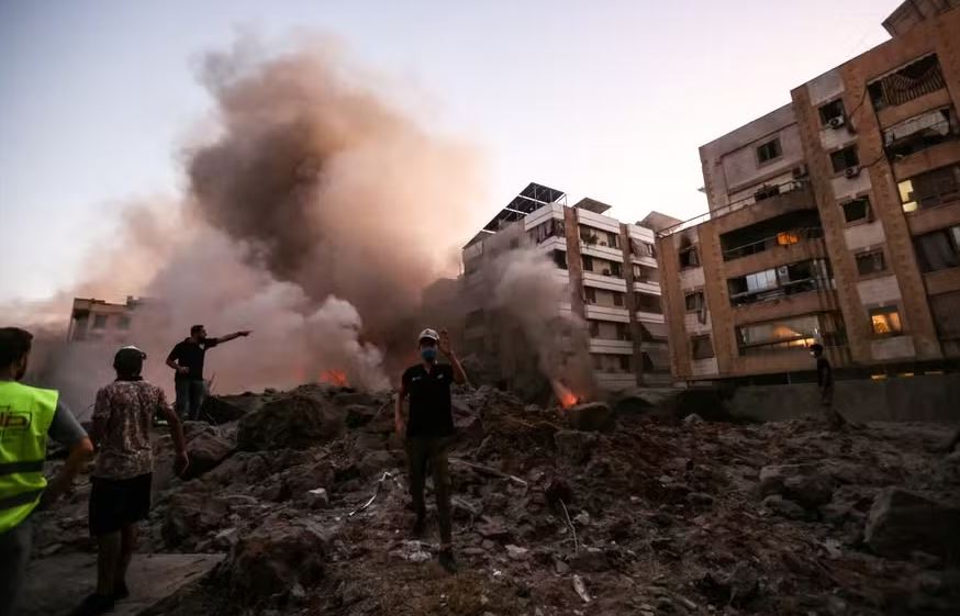 Pessoas e equipes de resgate em meio aos escombros de um prédio destruído em um ataque aéreo israelense no bairro de Haret Hreik, nos subúrbios ao sul de Beirute, em 27 de setembro de 2024 