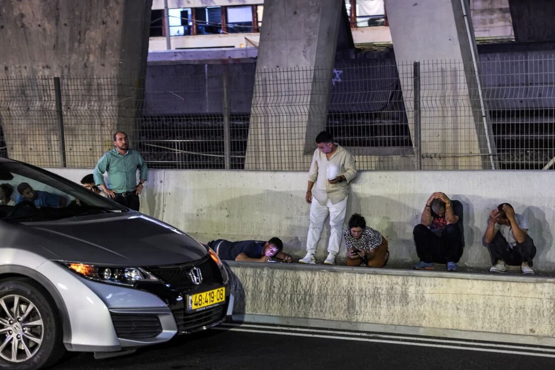 Pessoas se abrigam atrás de veículos sob uma ponte ao longo da lateral de uma rodovia em Tel Aviv