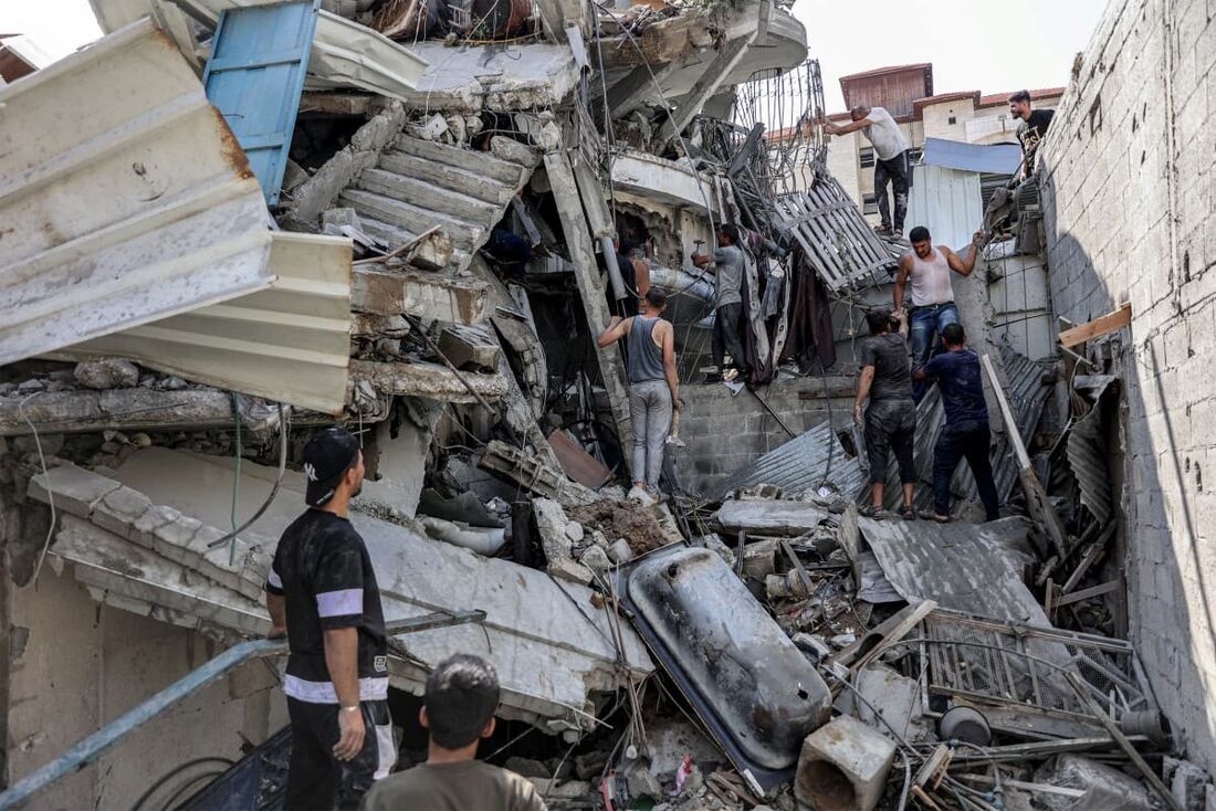 Pessoas se reúnem do lado de fora de um prédio desabado enquanto tentam resgatar um homem debaixo dos escombros após o bombardeio israelense no distrito de Saftawi, em Jabalia, no norte da Faixa de Gaza