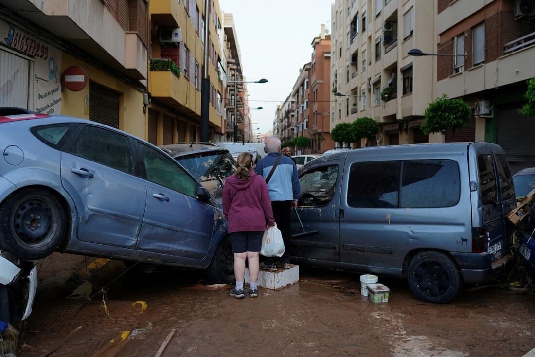 Moradores ficam em frente a carros empilhados após enchentes mortais no bairro de Alfafar, ao sul de Valência, leste da Espanha.