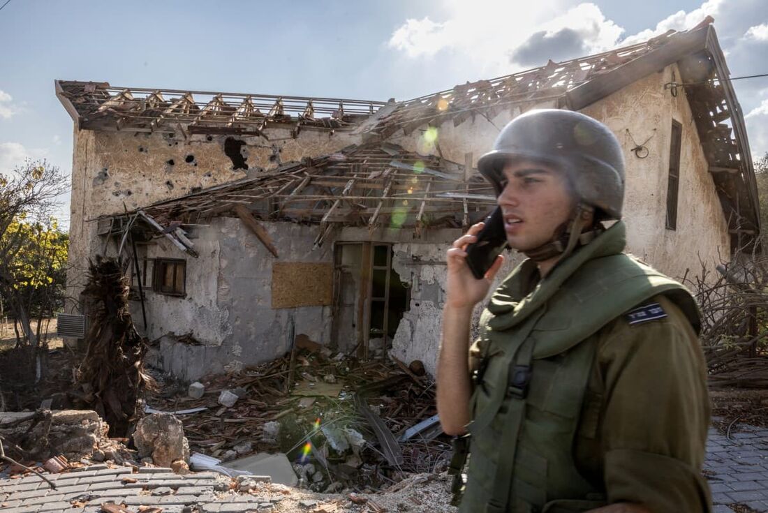 Um soldado israelense fala ao telefone em frente a uma casa atingida por foguetes do Hezbollah