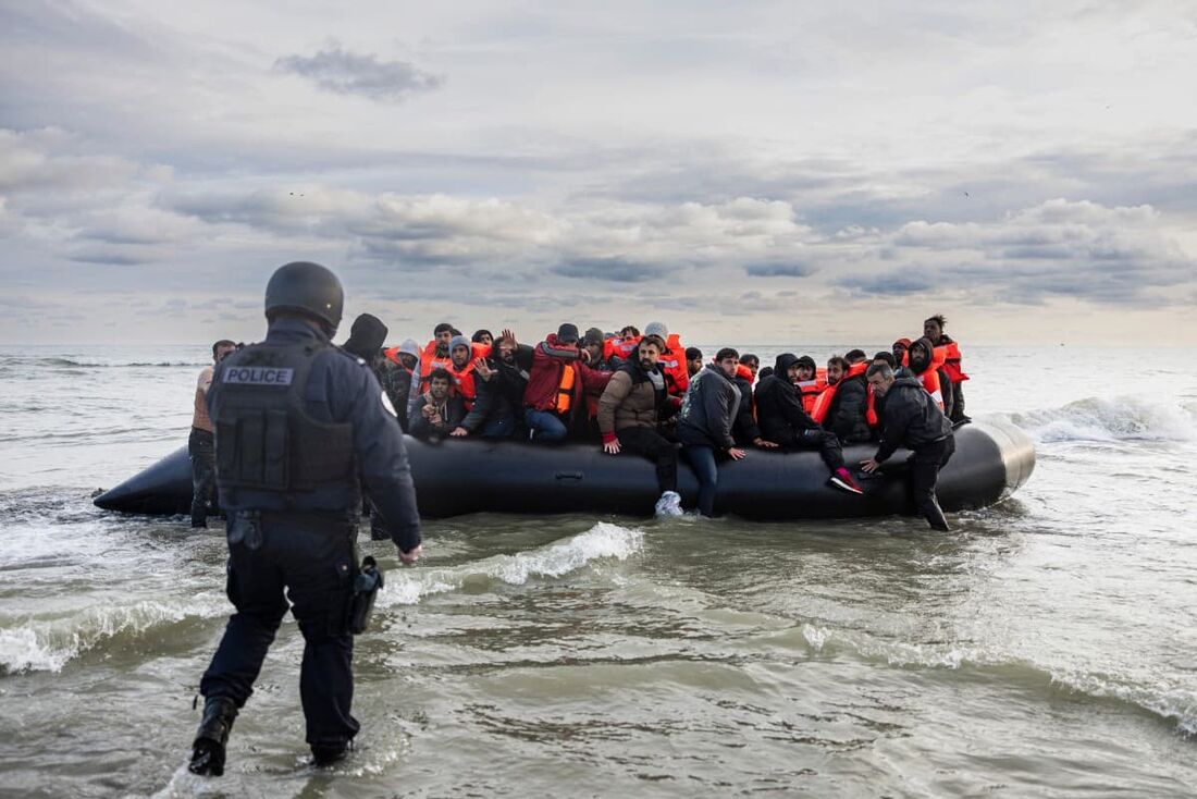  Migrantes reagem enquanto um policial francês está pronto para furar o barco do contrabandista com uma faca para impedir que migrantes embarquem em uma tentativa de cruzar o Canal da Mancha na praia de Gravelines.