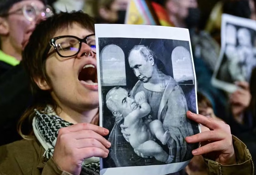 Manifestante segura uma imagem satírica da pintura 'Madonna and Child' de Da Vinci retratando o presidente da Rússia amamentando o candidato presidencial da Romênia, Catalin Georgescu, durante protesto 