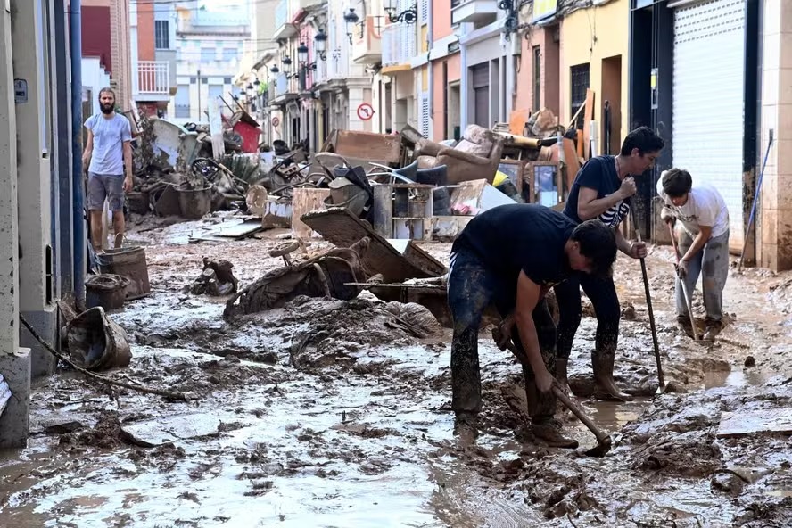 Pessoas tentam limpar uma rua coberta de lama em 31 de outubro de 2024 após enchentes repentinas afetarem Paiporta, em Valência, leste da Espanha 