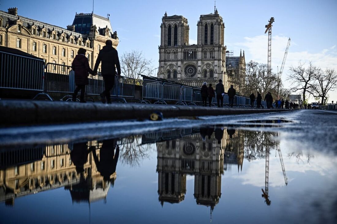 Pedestres passam pelas barreiras de segurança e cercas colocadas ao redor da catedral de Notre-Dame de Paris na véspera de sua reabertura oficial. 