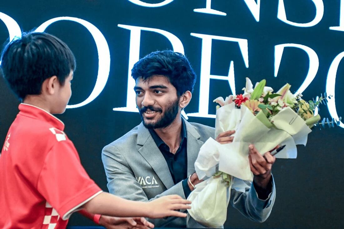 O campeão mundial de xadrez Gukesh Dommaraju (D) recebe um buquê de flores oferecido por um jovem fã durante uma sessão de meet and greet em Cingapura. 