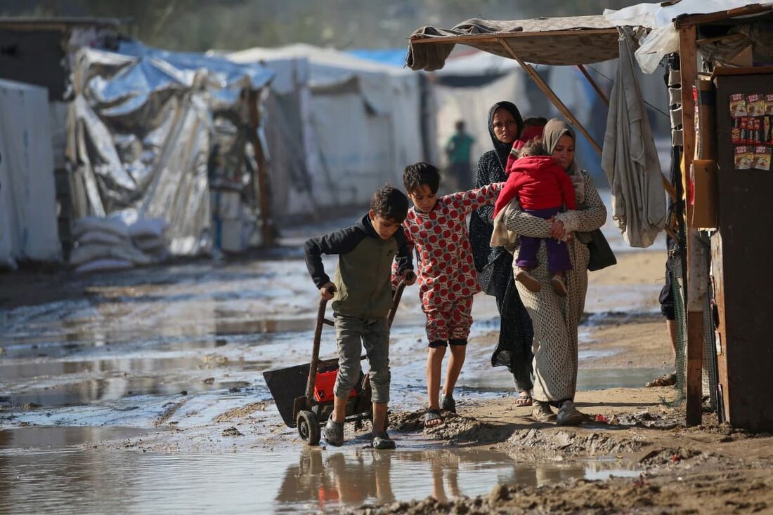 Pessoas caminham em uma área inundada após fortes chuvas em um campo de deslocados internos em Deir el-Balah, no centro da Faixa de Gaza.