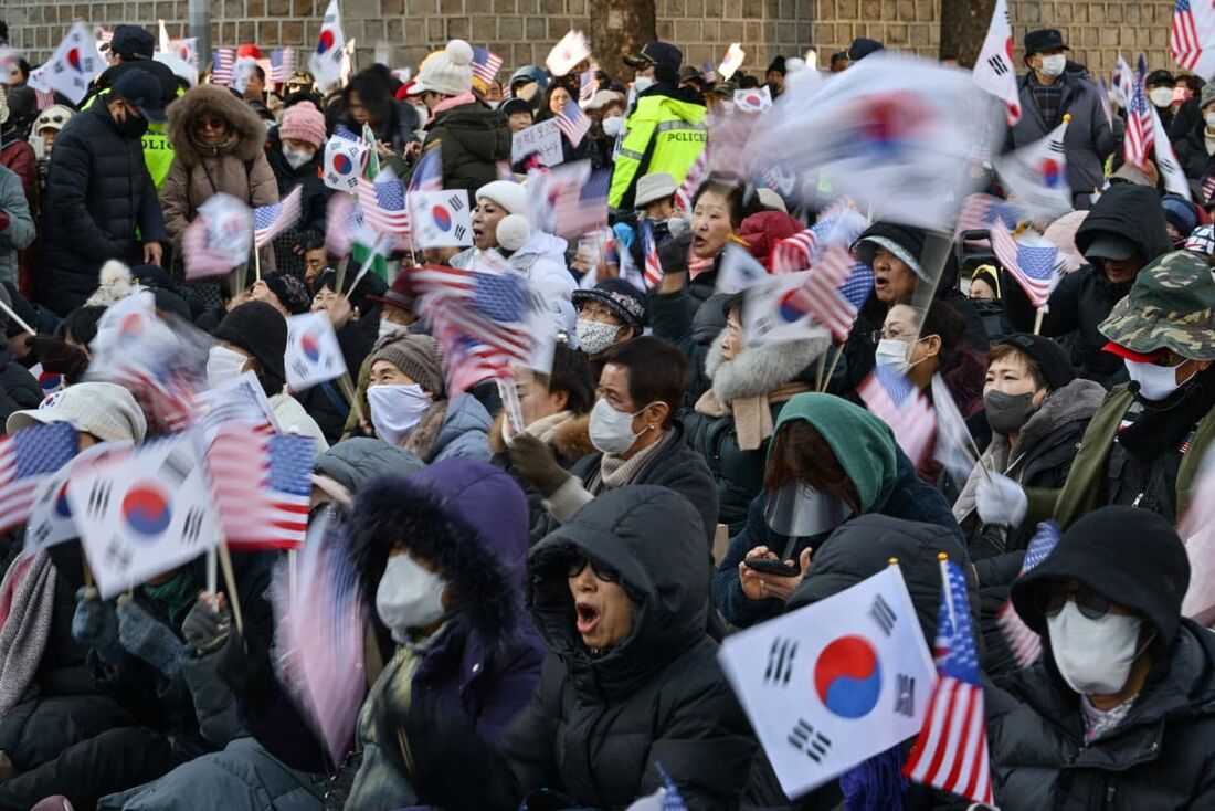 Pessoas agitam bandeiras da Coreia do Sul e dos EUA enquanto participam de um comício em apoio ao presidente Yoon Suk Yeol em Seul em 4 de dezembro de 2024. 