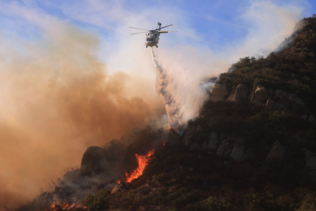 Um helicóptero joga água enquanto o inscêndio cresce em Malibu, Califórnia