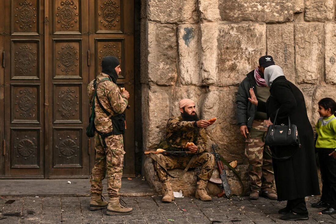 Um combatente oferece comida a uma mulher enquanto está sentado do lado de fora da mesquita Ummayad na cidade velha de Damasco