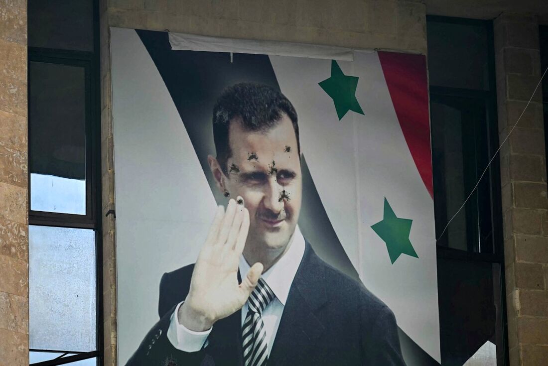 Um pôster crivado de balas do presidente sírio deposto Bashar al-Assad é retratado em Aleppo