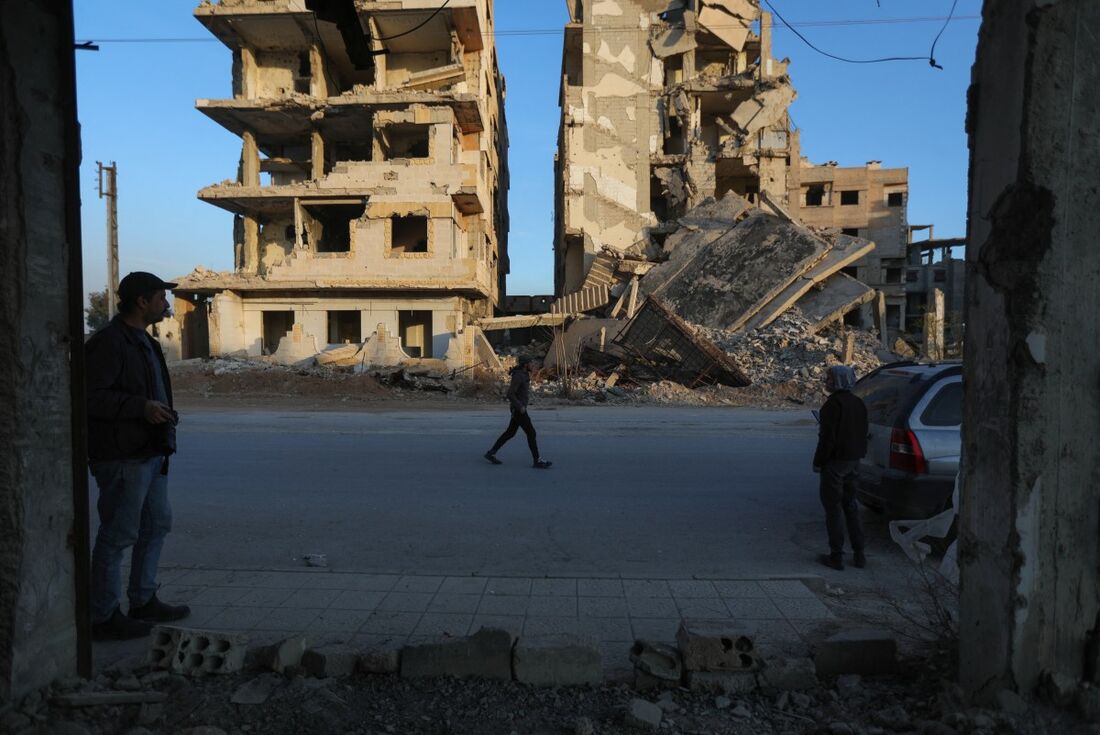 Pessoas diante de edifícios destruídos na cidade síria de Jobar