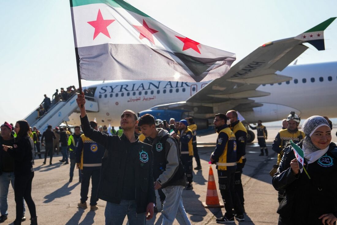 Um homem levanta uma bandeira síria da era da independência enquanto passageiros desembarcam de uma aeronave da Syria Air chegando de Damasco, no aeroporto da cidade de Aleppo