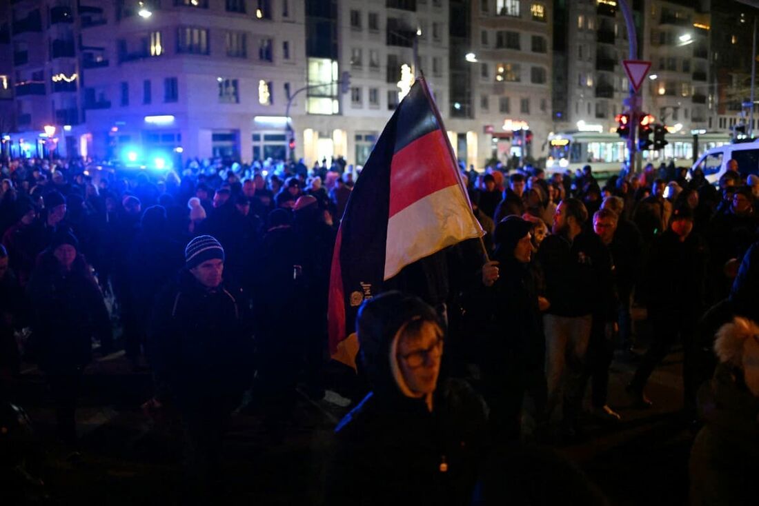 Pessoas caminham em uma "marcha fúnebre" e seguram uma bandeira com as cores alemãs. 