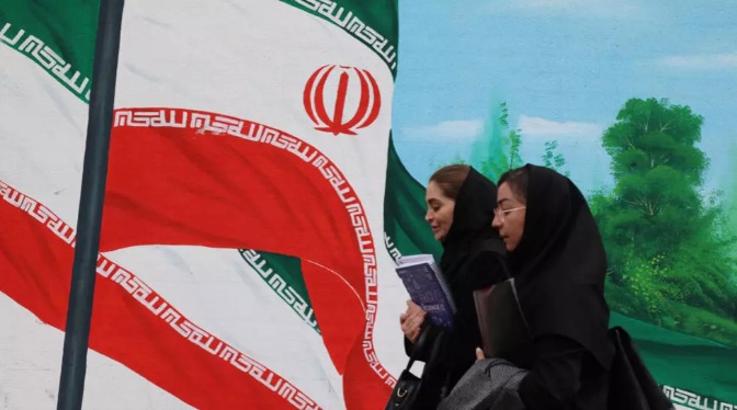 Mulheres iranianas passam por uma pintura mural de bandeiras iranianas em Teerã