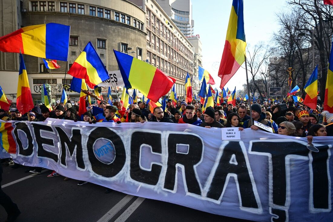 Apoiadores do partido nacionalista AUR (Aliança para a União dos Romenos) e do candidato presidencial Calin Georgescu seguram uma faixa com os dizeres "democracia" enquanto marcha em Bucareste em 12 de janeiro de 2024