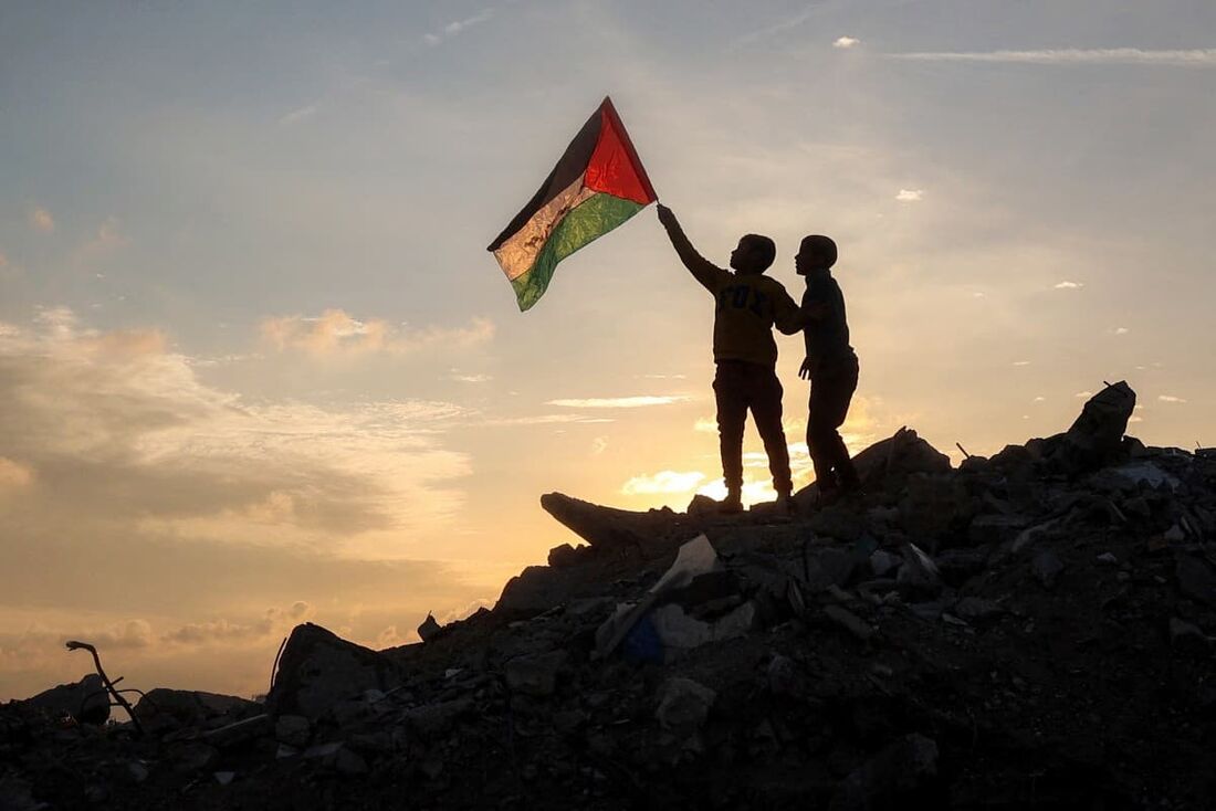  Um menino corre com uma bandeira palestina sobre um monte de escombros em um acampamento para pessoas deslocadas pelo conflito em Bureij, no centro da Faixa de Gaza