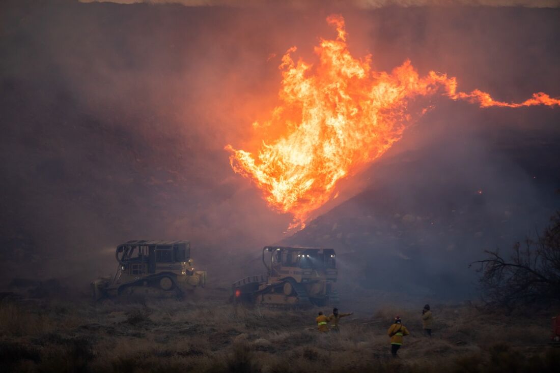 Um operador de escavadeira dirige-se às chamas para estabelecer uma linha de contenção para o incêndio 