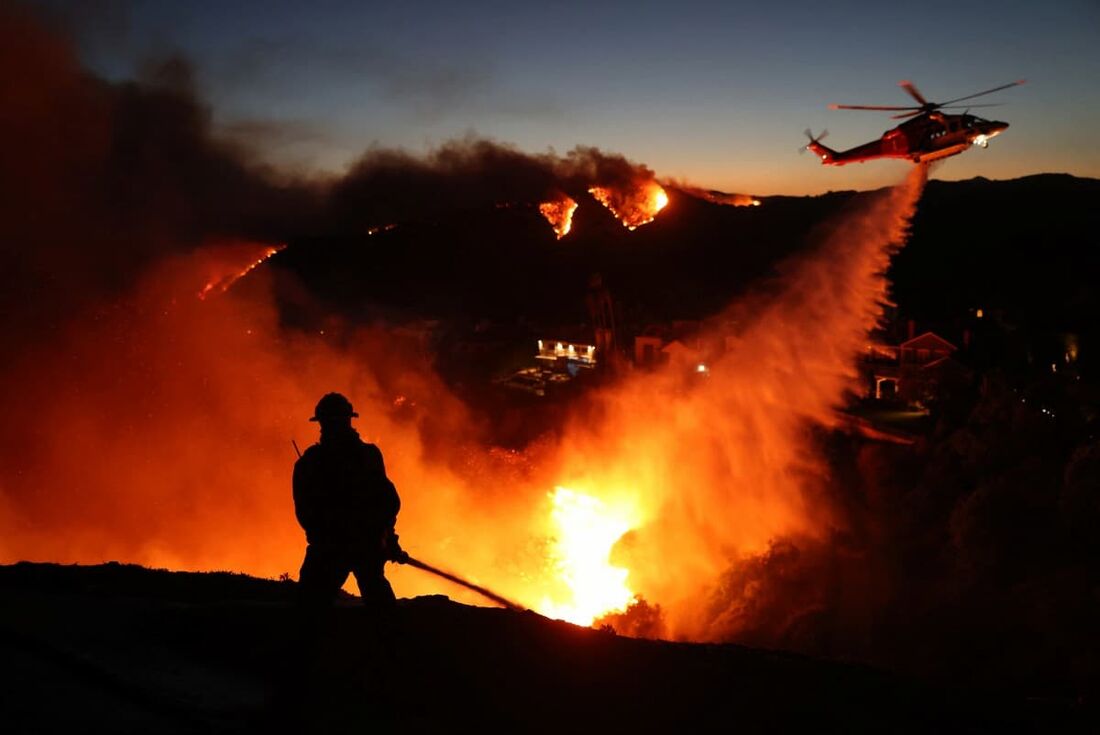  Bombeiros respondem a casas destruídas enquanto um helicóptero joga água enquanto o incêndio Palisades cresce em Pacific Palisades, Califórnia, em 7 de janeiro de 2025.