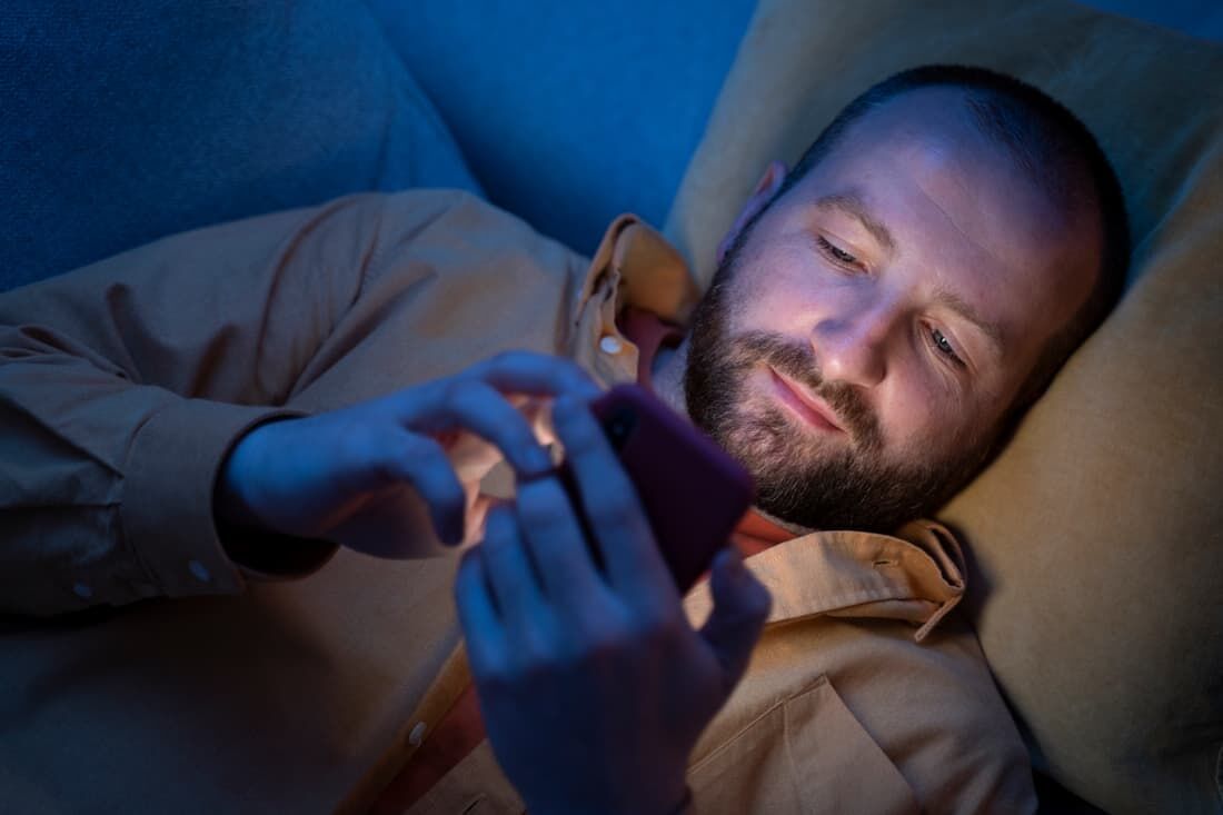 Homem mexendo no celular à noite