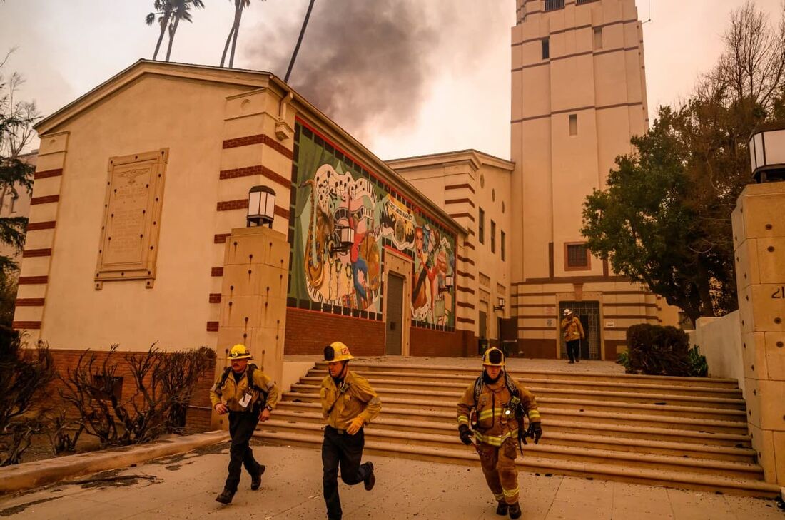 Bombeiros correm enquanto se preparam para combater as chamas no auditório da Eliot Arts Magnet Middle School enquanto a escola queima durante o incêndio de Eaton na área de Altadena, no condado de Los Angeles, Califórnia.